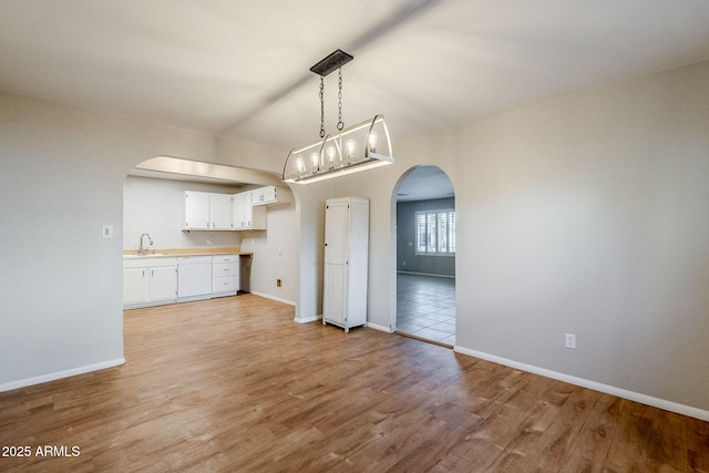 kitchen featuring white cabinets, dishwasher, light hardwood / wood-style floors, sink, and hanging light fixtures