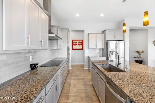 kitchen featuring decorative light fixtures, backsplash, appliances with stainless steel finishes, a sink, and dark stone counters