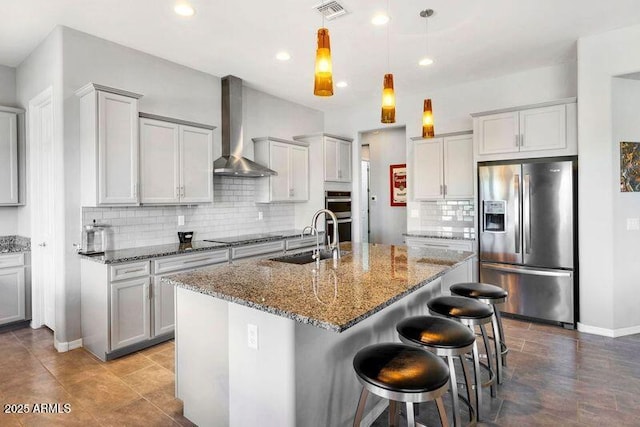 kitchen featuring a kitchen island with sink, stainless steel appliances, a sink, visible vents, and wall chimney range hood