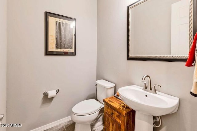 half bath featuring tile patterned floors, a sink, toilet, and baseboards