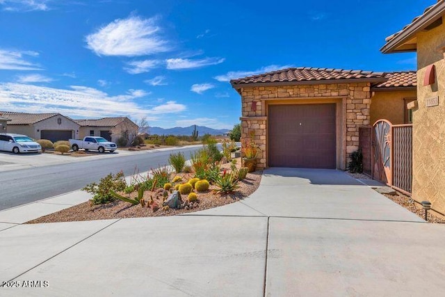 exterior space with a mountain view, a garage, stone siding, a tiled roof, and concrete driveway