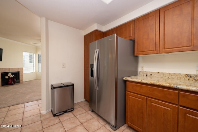 kitchen with light stone countertops, stainless steel fridge, light tile patterned flooring, and a fireplace