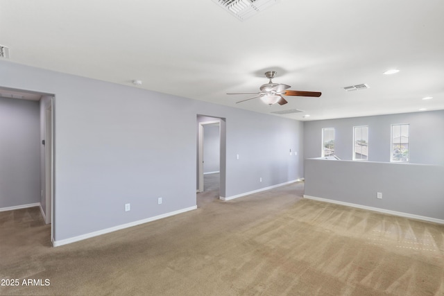 spare room featuring visible vents, light colored carpet, a ceiling fan, and baseboards