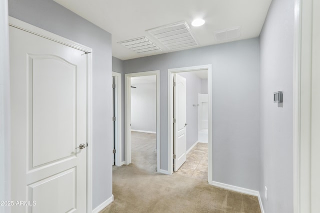 hallway featuring light colored carpet, visible vents, and baseboards