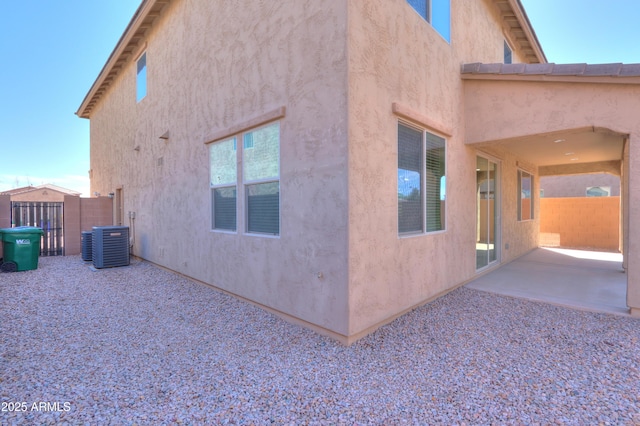 view of side of home featuring stucco siding, a patio, central AC, and fence