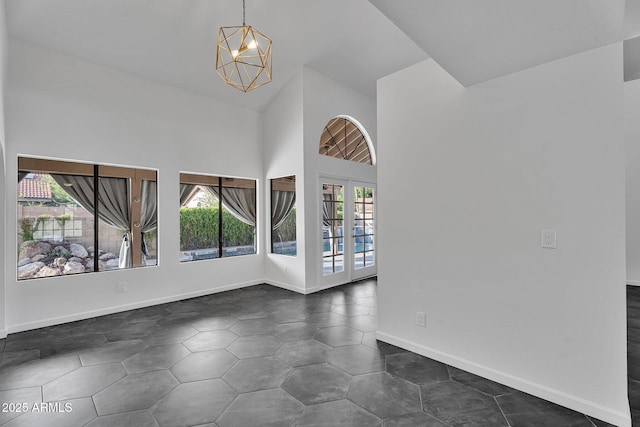 spare room featuring plenty of natural light, a chandelier, lofted ceiling, baseboards, and french doors