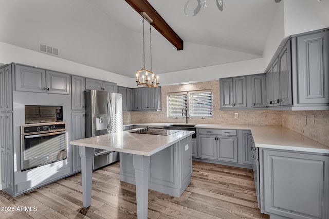 kitchen featuring gray cabinets, appliances with stainless steel finishes, a chandelier, a sink, and beamed ceiling
