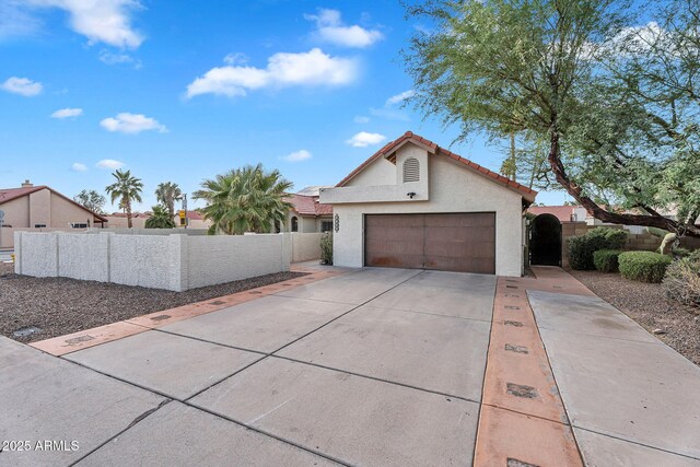 view of front of house featuring a garage, stucco siding, fence, concrete driveway, and a tiled roof