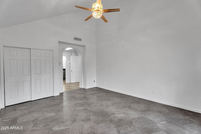 unfurnished bedroom with arched walkways, high vaulted ceiling, a closet, ceiling fan, and baseboards