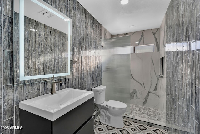 bathroom with tile walls, toilet, a marble finish shower, and vanity