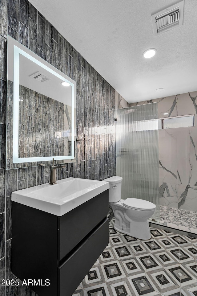 bathroom featuring tile walls, toilet, a stall shower, vanity, and a textured ceiling