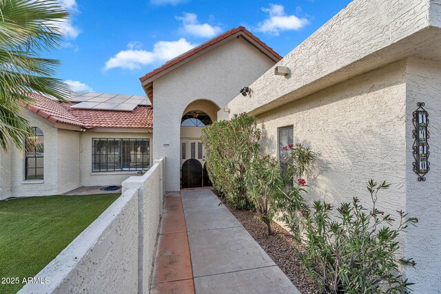doorway to property with stucco siding, solar panels, a tile roof, and a yard