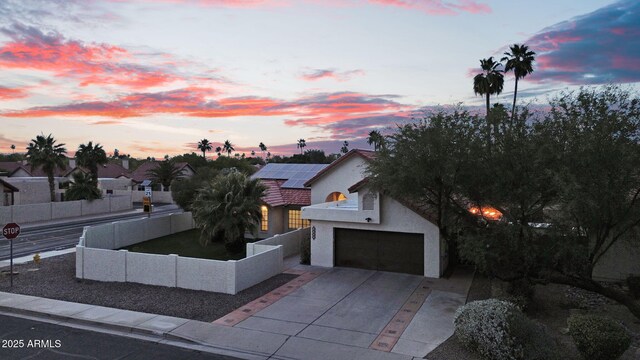 view of front of house with stucco siding, roof mounted solar panels, driveway, an attached garage, and a fenced backyard