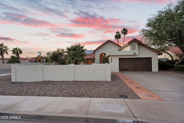 view of front of property with driveway, fence, stucco siding, and an attached garage