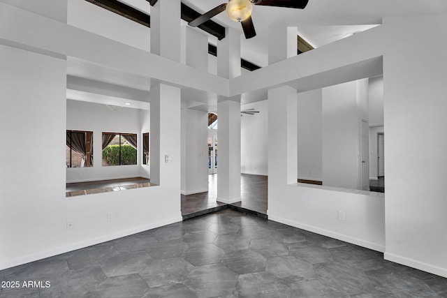 empty room with a ceiling fan, a towering ceiling, and baseboards