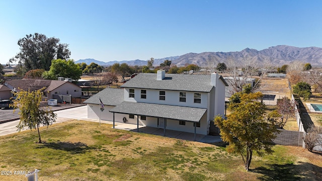 rear view of property featuring a mountain view, a patio area, and a lawn