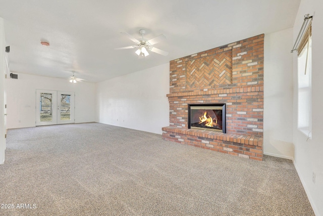 unfurnished living room with a brick fireplace, french doors, ceiling fan, and carpet flooring