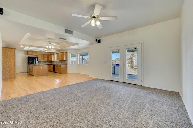 unfurnished living room with a raised ceiling, light colored carpet, ceiling fan, and french doors