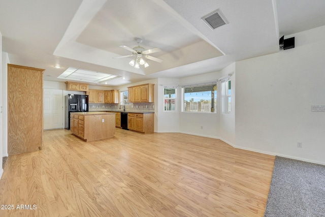 kitchen featuring backsplash, a tray ceiling, black appliances, a kitchen island, and light wood-type flooring