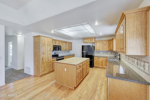 kitchen with sink, a center island, light wood-type flooring, appliances with stainless steel finishes, and dark stone counters