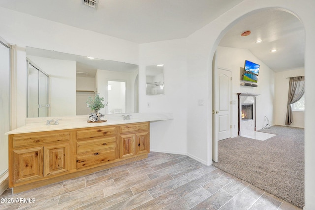 bathroom featuring vanity, lofted ceiling, a fireplace, and a shower with shower door