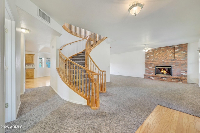 staircase featuring ceiling fan, a brick fireplace, and carpet