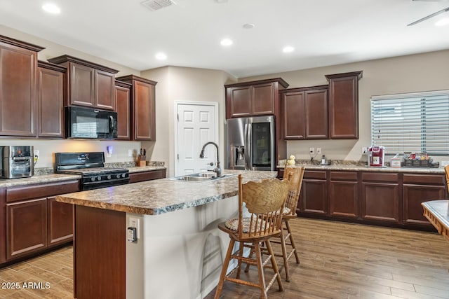 kitchen featuring sink, a breakfast bar area, light hardwood / wood-style flooring, an island with sink, and black appliances