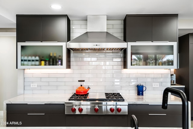 kitchen featuring wall chimney range hood, decorative backsplash, light stone countertops, and stainless steel gas cooktop