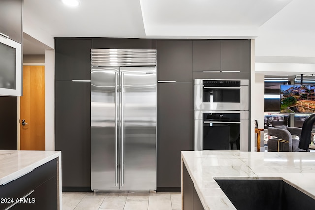 kitchen featuring appliances with stainless steel finishes, light stone countertops, light tile patterned flooring, and sink