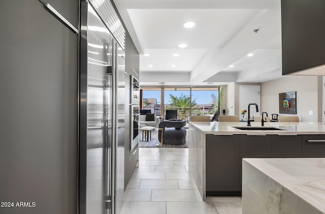 kitchen with light tile patterned flooring, light stone countertops, sink, and high end refrigerator