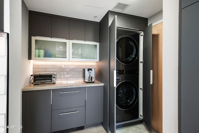 laundry area featuring stacked washer / drying machine and light tile patterned flooring