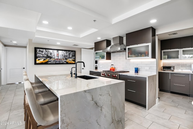 kitchen featuring wall chimney range hood, sink, a kitchen island, stainless steel gas stovetop, and a breakfast bar