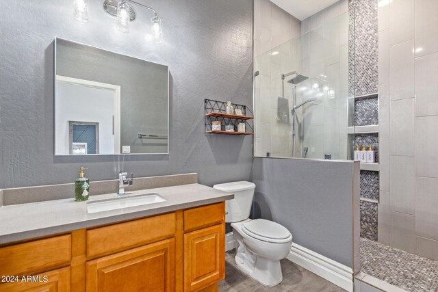 bathroom featuring vanity, wood-type flooring, a tile shower, and toilet