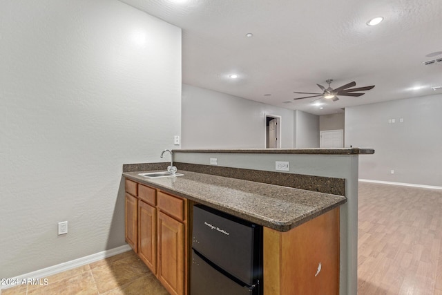 kitchen featuring sink, fridge, kitchen peninsula, ceiling fan, and dark stone counters