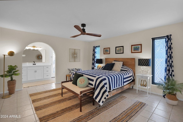 bedroom featuring connected bathroom, arched walkways, a sink, and light tile patterned floors