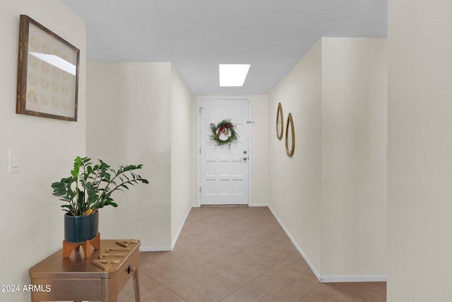 doorway to outside featuring a skylight, baseboards, and tile patterned floors