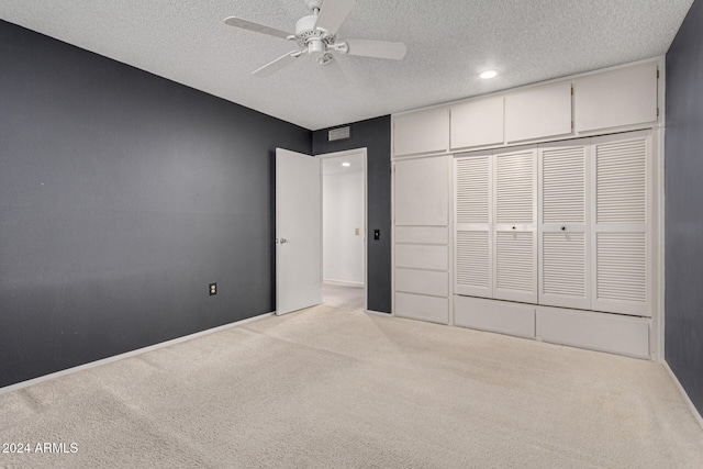 unfurnished bedroom with ceiling fan, light colored carpet, a textured ceiling, and a closet