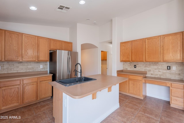41767 W Somerset Dr, Maricopa, AZ 85138 - kitchen featuring freestanding refrigerator, backsplash, an island with sink, arched walkways, and light countertops