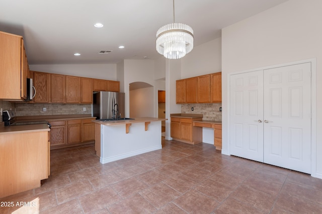 41767 W Somerset Dr, Maricopa, AZ 85138 - kitchen with stainless steel appliances, backsplash, arched walkways, a center island with sink, and a breakfast bar area