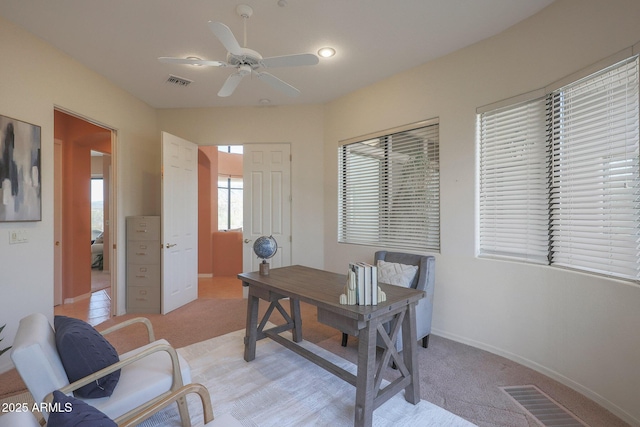 office space with light carpet, visible vents, and a ceiling fan