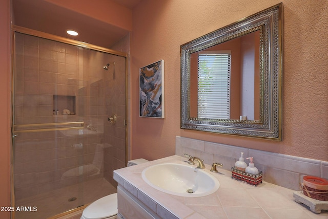 full bathroom featuring toilet, a stall shower, a textured wall, and vanity