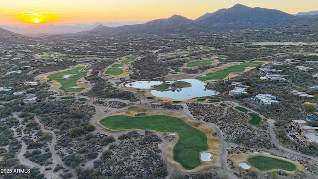 aerial view at dusk featuring view of golf course and a water and mountain view