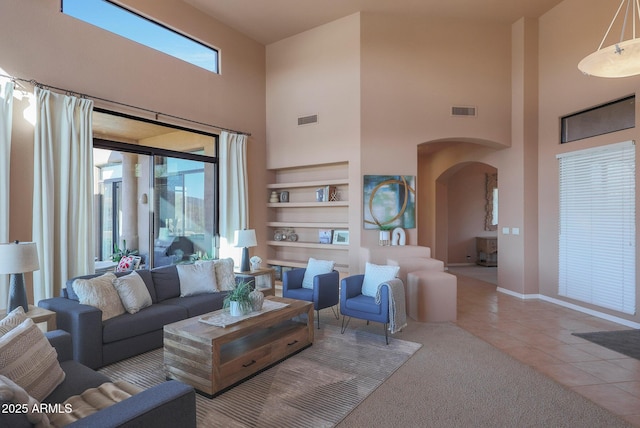 tiled living room with built in features, arched walkways, visible vents, and baseboards