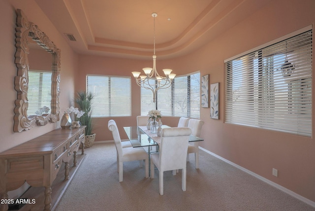 unfurnished dining area featuring carpet floors, a tray ceiling, visible vents, an inviting chandelier, and baseboards