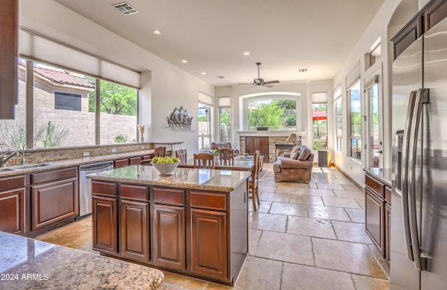 kitchen featuring sink, stainless steel appliances, a center island, a fireplace, and light stone countertops