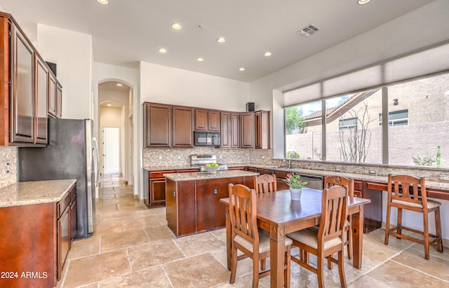 kitchen with stainless steel appliances, a kitchen island, backsplash, and light stone counters