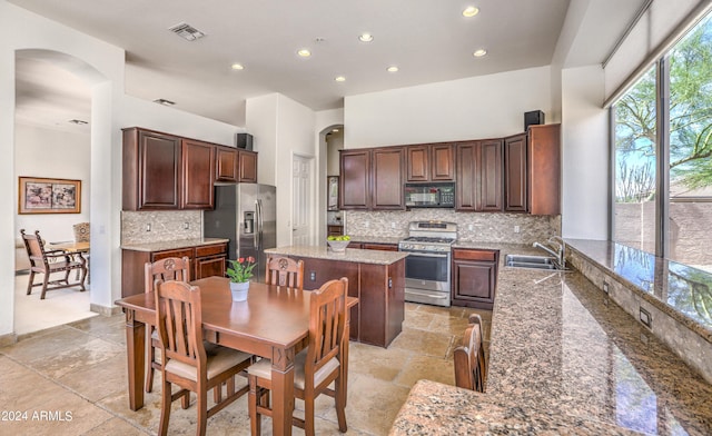 kitchen with sink, stainless steel appliances, tasteful backsplash, light stone countertops, and a kitchen island