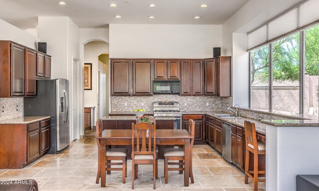 kitchen with sink, decorative backsplash, a center island, light stone counters, and stainless steel appliances