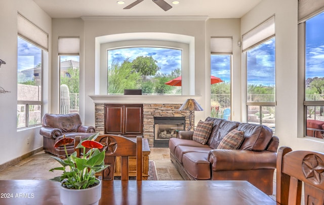 sunroom featuring a stone fireplace and ceiling fan