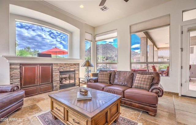 interior space featuring ceiling fan, ornamental molding, plenty of natural light, and a stone fireplace